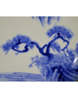Close-up of blue and white hand painted porcelain plate with mountain landscape and willow trees detailing.