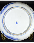 Close-up of the underside of a white porcelain plate with blue mountain landscape, blue stamp, on brass stand.