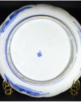Close-up of the underside of a white porcelain plate with blue mountain landscape, blue stamp, on brass stand.