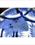 Close-up of antique hand painted porcelain plate featuring pine cone cluster and dense foliage motif.