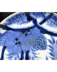 Close-up of antique hand painted porcelain plate featuring pine cone cluster and dense foliage motif.
