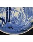 White porcelain plate with hand painted pine cone cluster and dense foliage, displayed on brass stand.