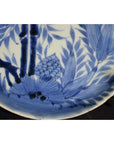 White porcelain plate with hand painted pine cone cluster and dense foliage, displayed on brass stand.