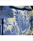 Close-up of antique Asian porcelain plate with hand painted pine cone cluster and dense green foliage details.