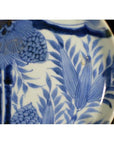 Close-up of antique Asian porcelain plate with hand painted pine cone cluster and dense green foliage details.