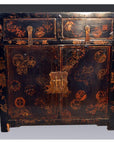 Black lacquer Chinese wood cabinet with gold details, red floral motifs, two drawers, and scalloped metal hardware.