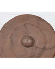 Bronze Burmese temple gong with raised center and red mallet, set against a white brick wall.