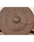 Bronze Burmese temple gong with raised center and red mallet on stand against white brick wall.