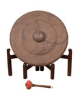 Bronze Burmese temple gong with raised center on stand, red mallet in front, close-up view.