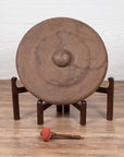 Bronze Burmese temple gong with raised center, red mallet, on wooden stand, close-up.