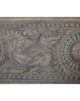 Brown wooden Indian carving of a stylized bird with intricate circular and floral patterns, close-up view.