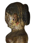 Weathered wooden statue of a woman with hair in a bun, side view.