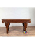 Dark wood Chinese altar console table with carved scrollwork, overhang top, on wood floor against white brick wall.