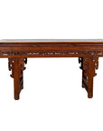 Dark wood Chinese altar console with overhang top and open fretwork scrolls, placed by a white brick wall on wooden floor.