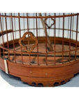 Close-up of an antique Chinese bird cage with vertical metal bars and quatrefoil accent, warm brown finish.