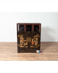 Black lacquered wood Chinese display cabinet with hand painted chinoiserie and open shelf, against white brick wall.
