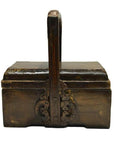 Brown wooden Chinese dowry box with curved handle and ornate carved metal accents on the front, close-up view.