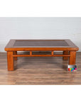 Brown Chinese Elm coffee table with square legs and rattan inset top, on wood floor with color card nearby.