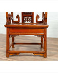 Natural wood antique hand-carved Chinese chair on wooden floor against white brick wall indoors.