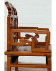 Brown wood chair with ornate hand-carved scrollwork, side view, showing natural wood patina.
