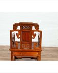 Brown wood hand-carved chair with natural patina, back view, against white wall and wood floor indoors.