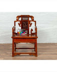 Natural wood chair with hand-carved details, wood patina, on wooden floor by white brick wall, color card on seat.