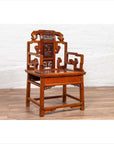 Brown wood hand-carved antique Chinese chair with natural patina on wood floor, white brick wall background.
