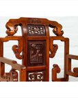 Brown wood hand-carved Chinese chair with geometric armrests and natural patina, set indoors against a white brick wall.