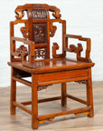 Brown wood hand-carved chair with natural patina on a wooden floor against a white wall indoors.