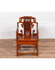 Brown wood hand-carved chair with natural patina on a wood floor in front of a white brick wall indoors.