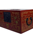 Red Chinese lacquer box with gilt vine and phoenix motif, black handles, and decorative black latch, close-up view.