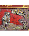 Red lacquer wood box with gilt gold floral inlay and carved wood details beneath trees, on plain background.