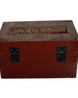 Red and gold lacquer box with raised top scene and ornate vintage details, on plain background.