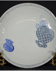 Close-up of an antique Chinese porcelain plate with hand painted blue fish, embossed details, on ornate gold stand.