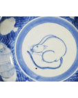White ceramic scalloped dish with central crouching mouse and barrel cartouche, ornate decorative borders, close-up.