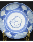 Blue and white ceramic scalloped dish with crouching mouse and barrel design, displayed on a stand.