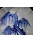 White porcelain fluted plate with scalloped edge, featuring detailed wind-swept pine design, close-up view.