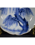 White porcelain fluted plate with Wind-Swept Pine design on decorative brass stand, close-up.