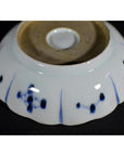 White and blue porcelain fluted plate with wind-swept pine and floral patterns, smooth unglazed base, close-up view.