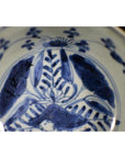 Close-up of antique Asian porcelain dish with foliate hill motif, rustic brushwork, and a small surface crack.