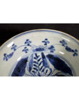 Close-up of a white porcelain Asian dish with foliate hill motif and rustic brushwork on a dark background.
