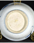 White porcelain dish with foliate hill motif, bottom view, displayed on ornate brass stand.
