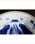 Close-up of blue and white porcelain dish with radial botanical spray pattern on rim, antique Asian style.