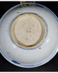 Close-up of the underside of a blue porcelain Asian dish with botanical spray pattern, rough base, on black background.