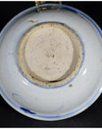 Close-up of the underside of a blue porcelain Asian dish with botanical spray pattern, rough base, on black background.