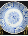 White porcelain bowl with butterfly cartouches and petal rim, on ornate brass stand against a dark background.
