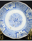 White porcelain bowl with butterfly cartouches and petal rim, on ornate brass stand against a dark background.