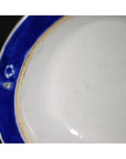 Close-up of antique Asian plate with broad blue rim, minimal white center, small mark visible on rim edge.