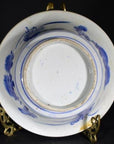 Close-up of an antique Asian deep plate with a broad blue rim, minimal center, on a gold stand against a dark background.