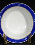 Blue-rimmed antique Asian deep plate on gold stand, black background, ceramic tableware close-up.